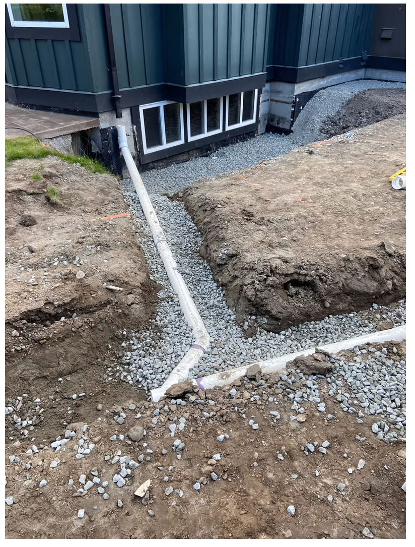 Residential perimeter drainage trench filled with clear crush rock and drain pipe beside a foundation wall