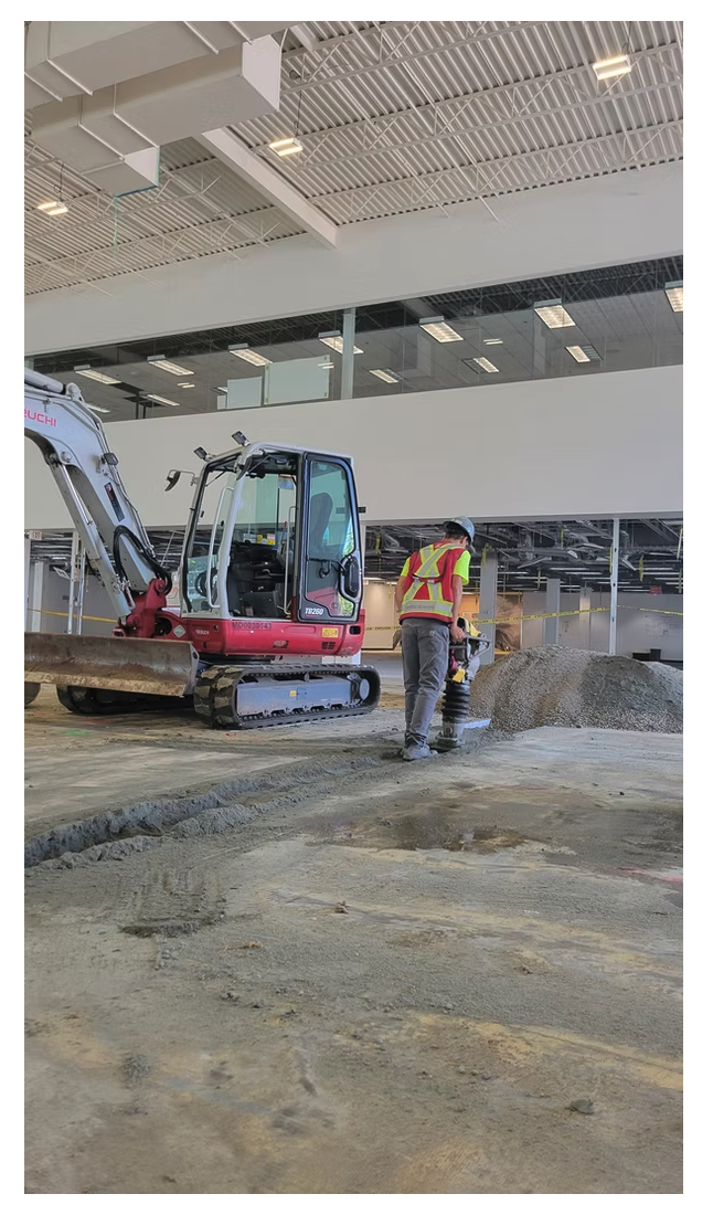 Radius Excavation crew compacting gravel base inside a commercial interior with a Takeuchi mini excavator, Vancouver BC