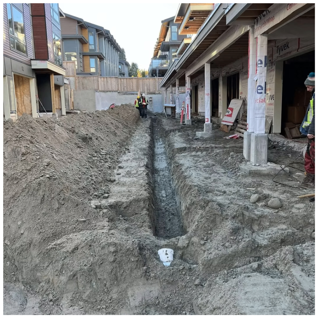 Long deep utility trench between new townhouse buildings with a construction crew supervising the run