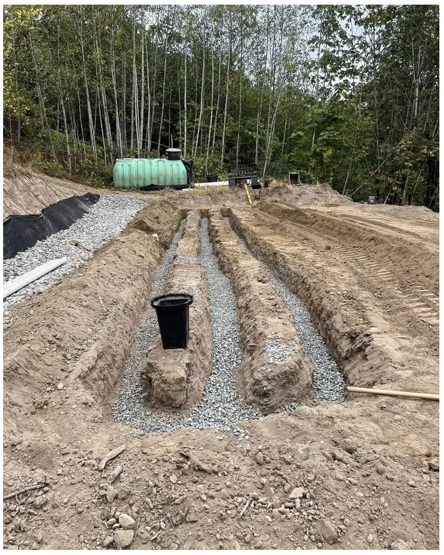 Newly installed septic drain field with gravel-filled trenches, distribution box and holding tank in a wooded rural lot