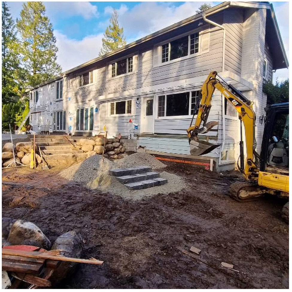CAT excavator grading a backyard with new granite stone steps and boulder retaining wall at a Lower Mainland home