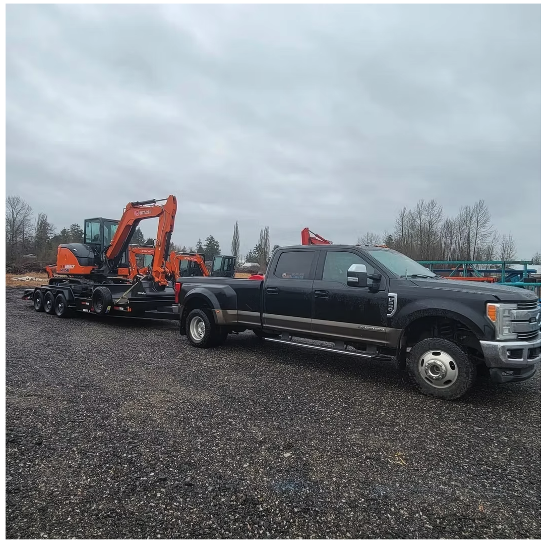 Heavy-duty pickup towing multiple excavators on a trailer across a gravel yard
