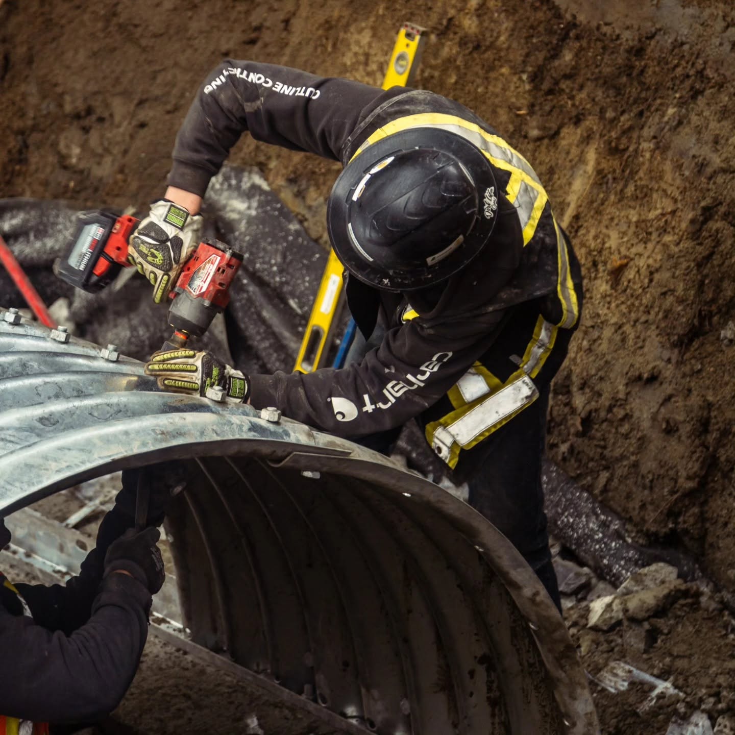Radius Excavation crew member torquing bolts on a large corrugated metal culvert inside a deep trench