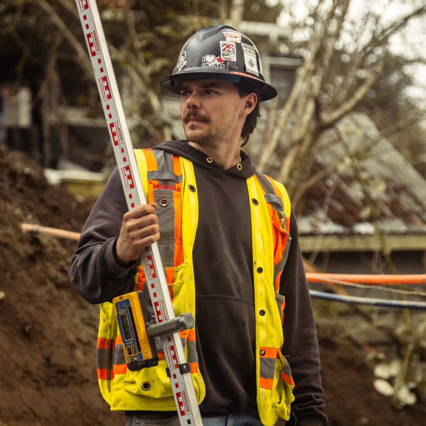 Radius Excavation surveyor holding a laser grade rod with receiver on a residential site preparing for elevation checks