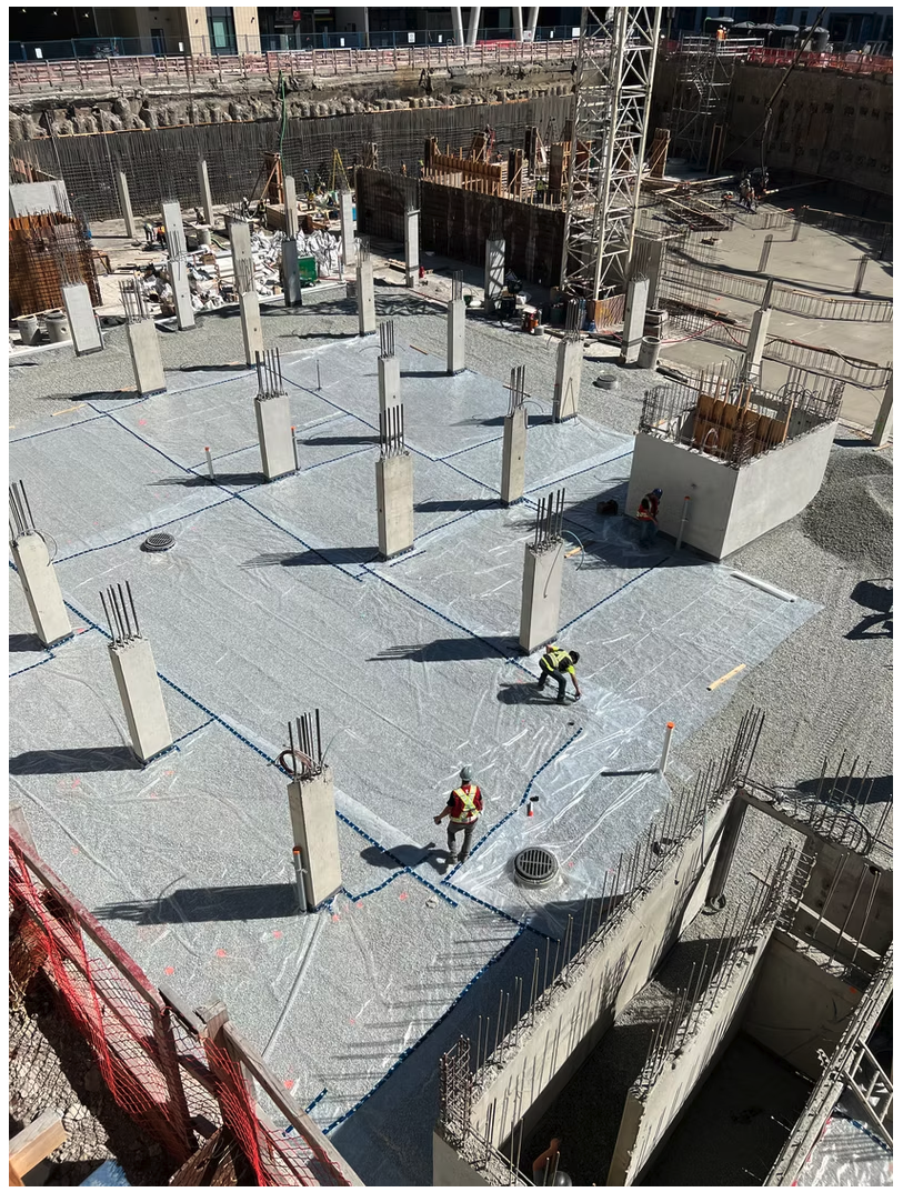 Compacted gravel base with vapour barrier and rebar column starters ready for slab-on-grade pour