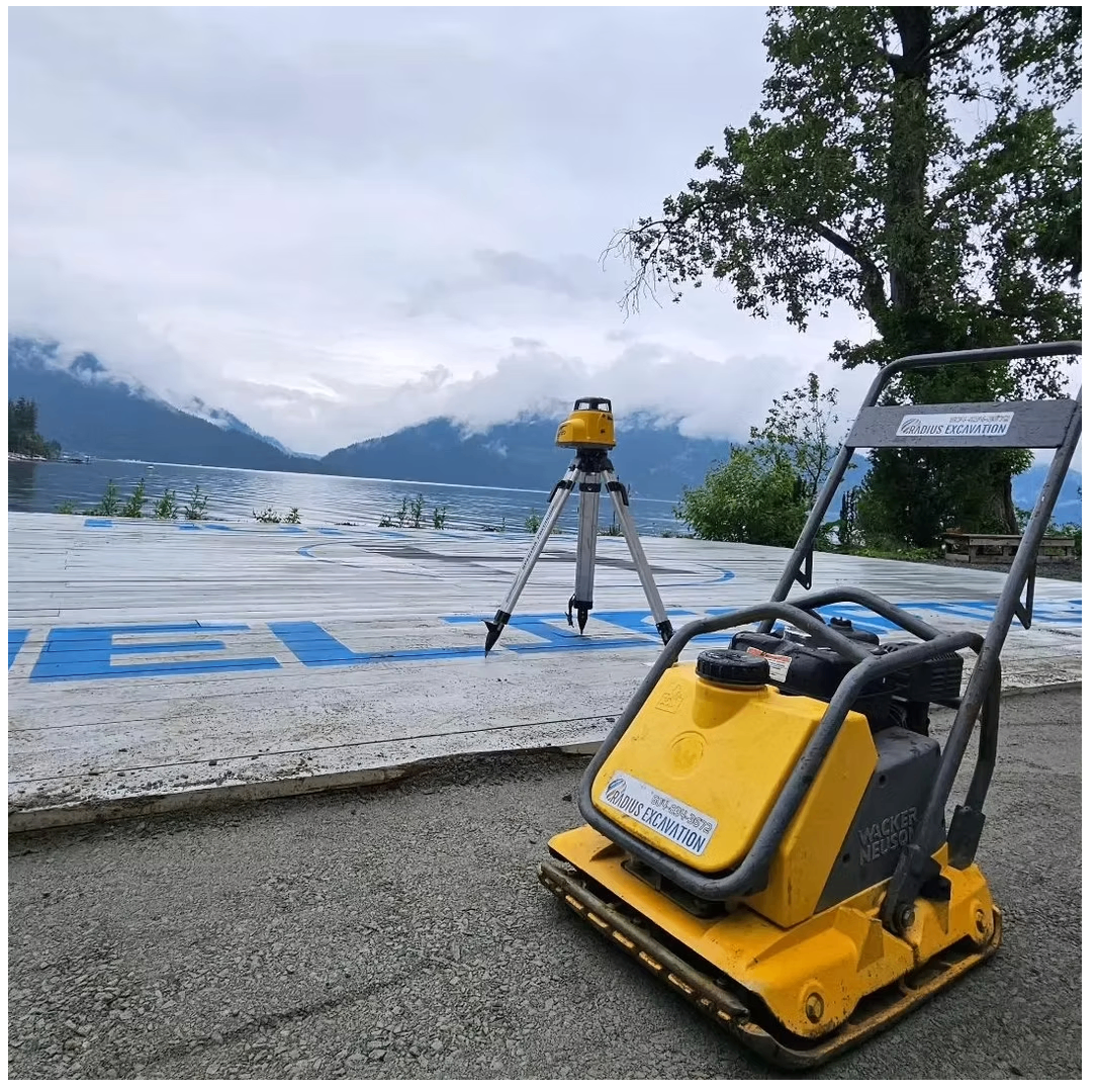 Radius Excavation Wacker Neuson plate compactor and rotary laser level on a lakeside pad under moody mountain clouds