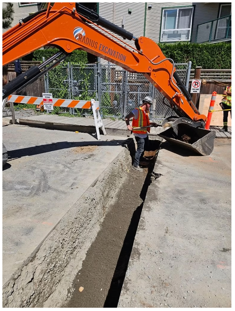 Crew and Radius Excavation mini excavator digging a utility trench across a Vancouver street with traffic control