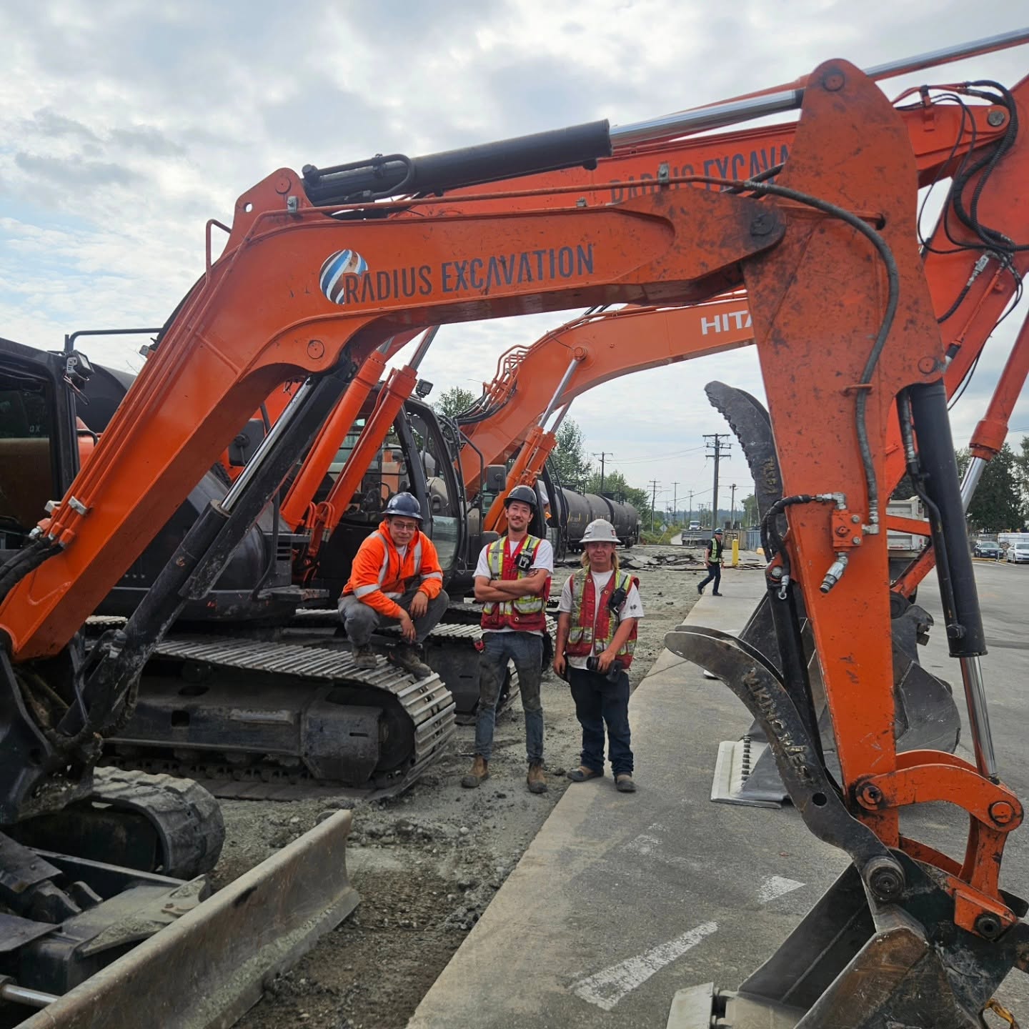 Radius Excavation team standing between two branded Hitachi excavators at a rail utility crossing project