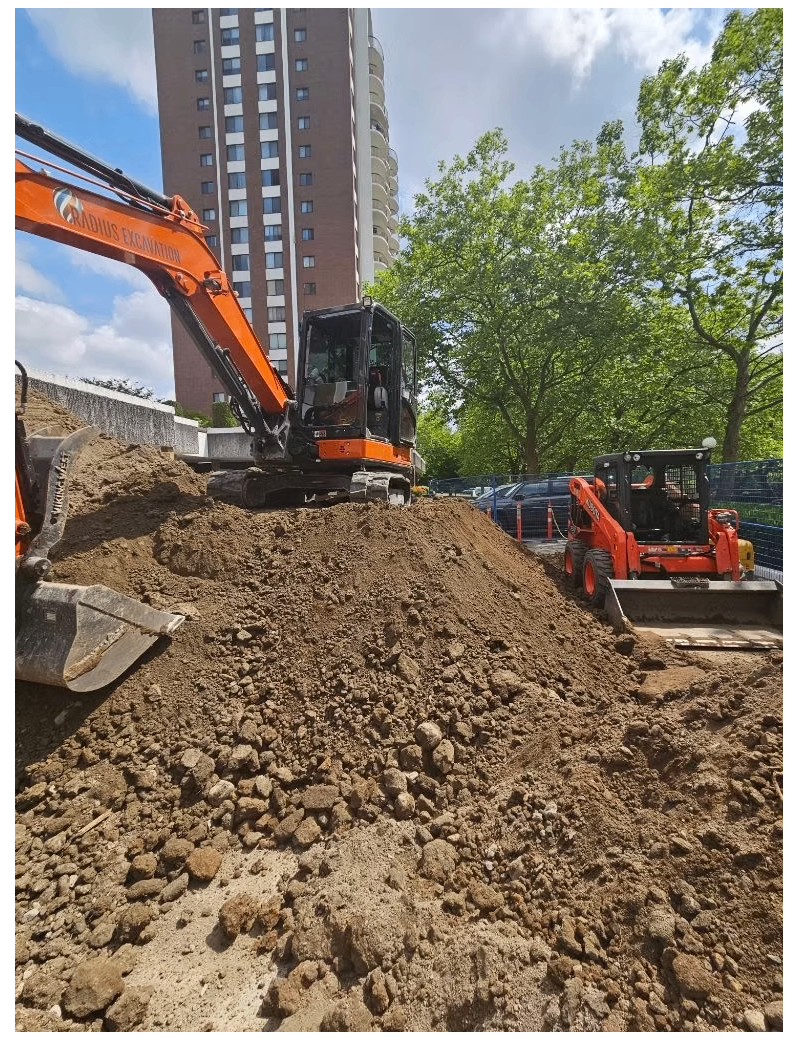 Radius Excavation mini excavator and Kubota skid steer moving soil beside a downtown Vancouver high-rise