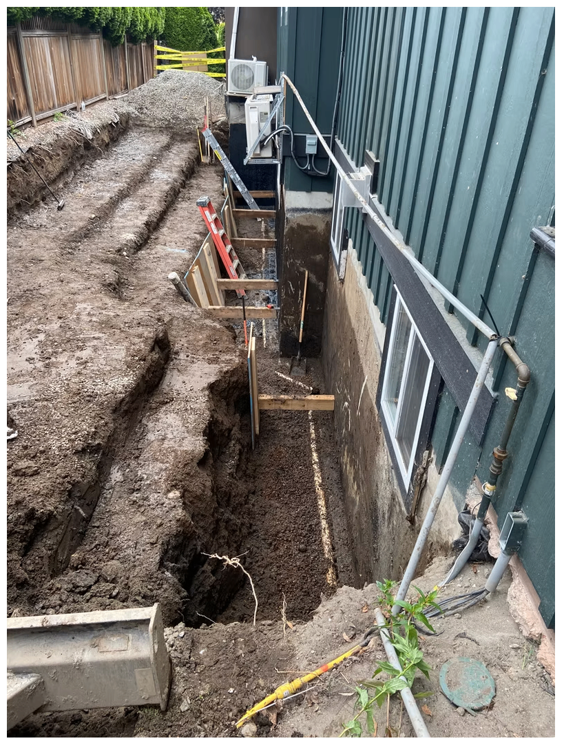Deep narrow excavation along a house foundation for waterproofing and drainage upgrades